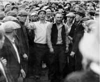 Tacoma and Seattle longshoremen lead a strikebreaker, identified as 'Iodine' Harradin, off the Seattle docks. Harradin and other strikebreakers were removed under a flag of truce as police stood back. The striker with right arm upraised is Phil Green, Seattle. Port of Seattle photo. Ronald E. Magden Collection.